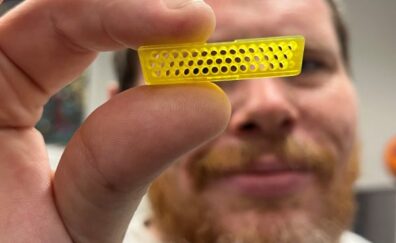Ben Dopp holding a small yellow micro 3D printed connector part with three rows of tiny through-holes